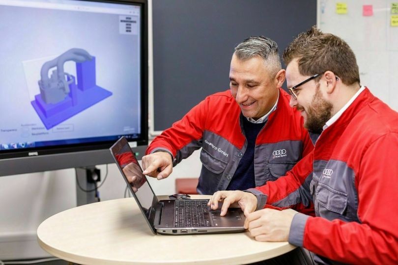 Two men who are part of the Audi 3D printing team look at a laptop. 